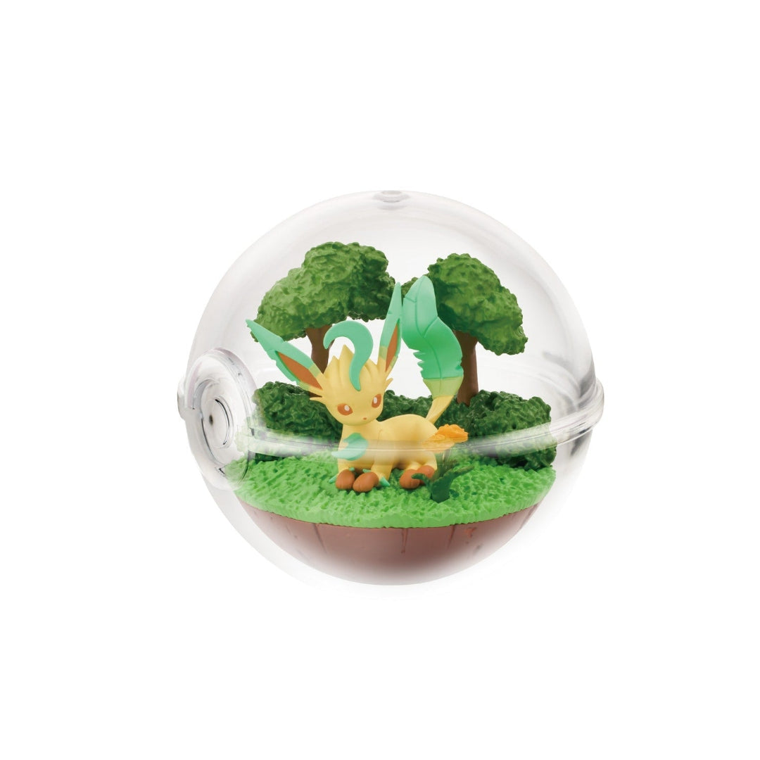 A small figure of Leafeon from Pokémon lying down in a forest-themed scene inside a clear Poké Ball-shaped case. The background features green grass, bushes, and leafy trees, creating a peaceful woodland setting.