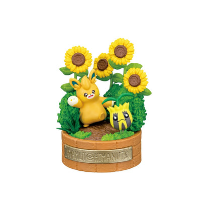 A small Pokémon figure featuring Pawmot standing with an expressive pose beside Sunkern, surrounded by tall sunflowers and green bushes. The display rests on a round, light brown base. 