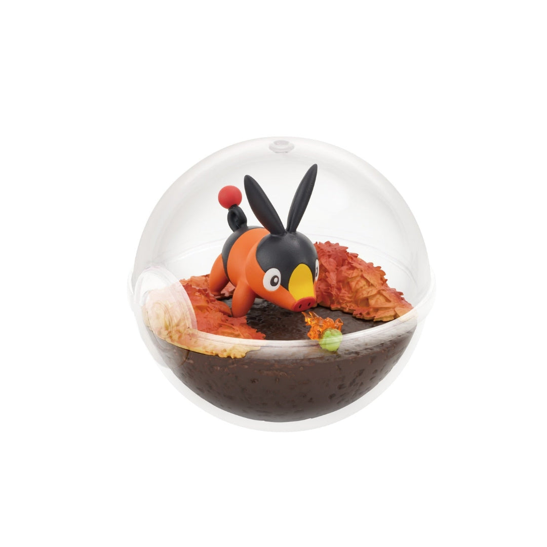 A small terrarium-style figure of Tepig from Pokémon inside a clear Poké Ball-shaped case. Tepig is shown playfully snorting a small flame near a green caterpillar, surrounded by autumn-colored leaves on dark brown terrain.