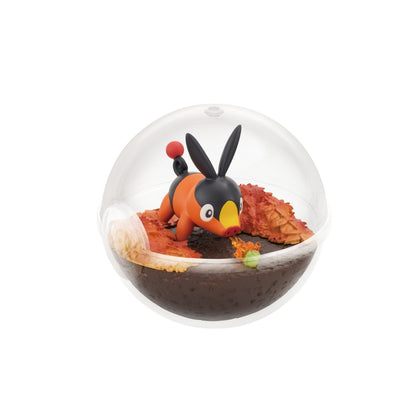 A small terrarium-style figure of Tepig from Pokémon inside a clear Poké Ball-shaped case. Tepig is shown playfully snorting a small flame near a green caterpillar, surrounded by autumn-colored leaves on dark brown terrain.
