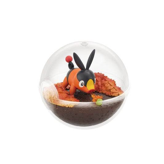 A small terrarium-style figure of Tepig from Pokémon inside a clear Poké Ball-shaped case. Tepig is shown playfully snorting a small flame near a green caterpillar, surrounded by autumn-colored leaves on dark brown terrain.