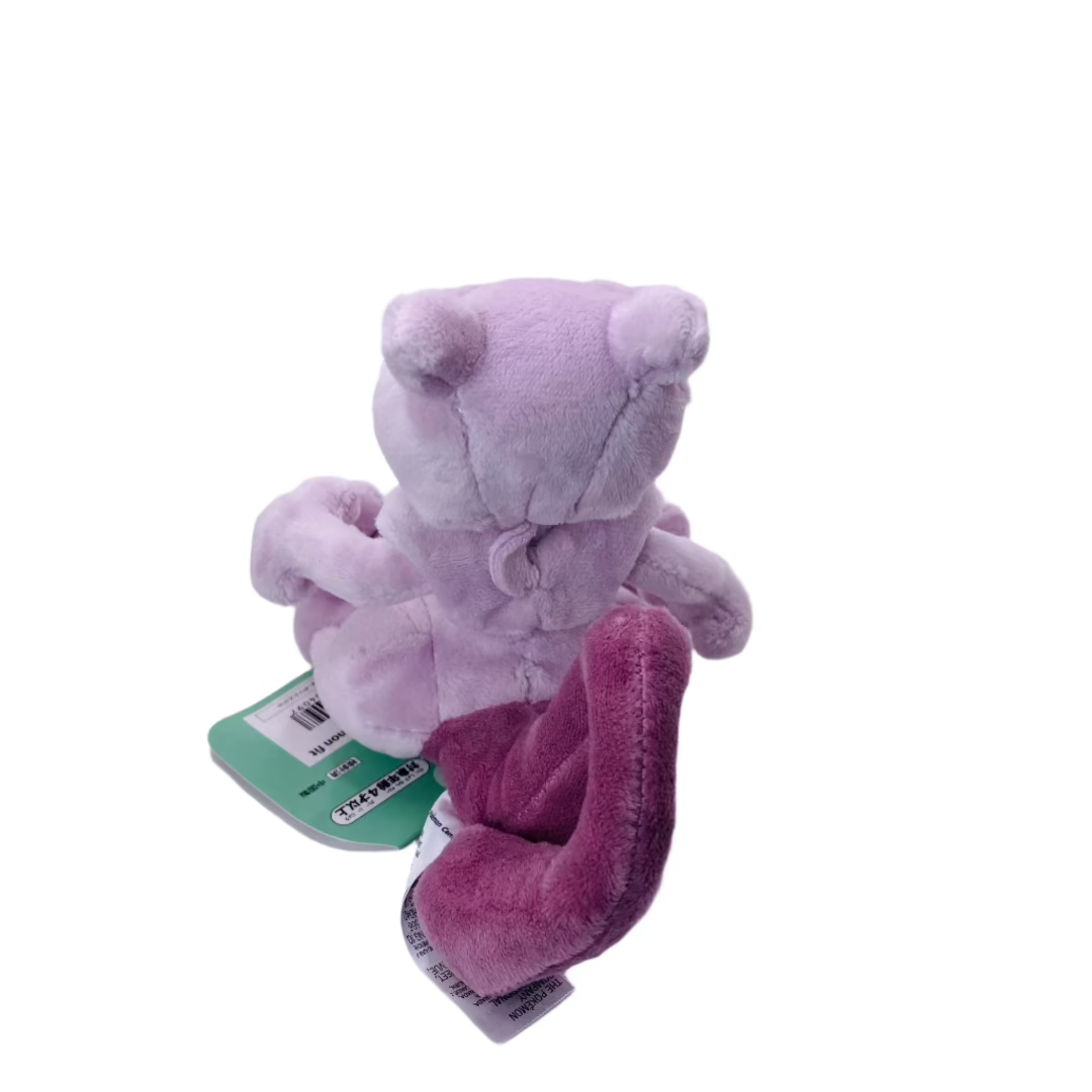 Back view of a Mewtwo plush toy from Pokémon, showing its long purple tail extending from the base, rounded head with ear-like projections, and smooth light gray fabric.