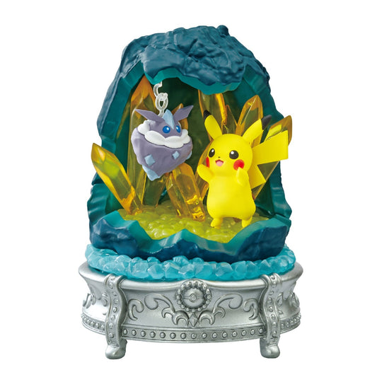 A detailed Pokémon figure featuring Pikachu standing in front of glowing yellow crystals inside a rocky cave. Above Pikachu, Carbink is suspended in midair. The scene sits atop a silver, ornate pedestal with blue gem-like decorations.